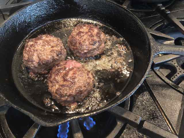 Wagyu beef sliders slowly releasing their fat in a cast-iron skillet.